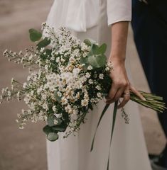 a close up of a person holding a bouquet of flowers and greenery in their hands