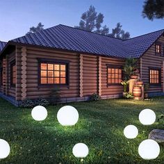 the lights are on in front of the log cabin style house at night, with grass and rocks scattered around it