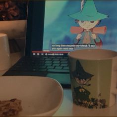 a laptop computer sitting on top of a desk next to a cup and saucer