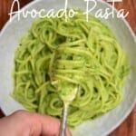 a person is holding a spoon over a bowl of green pasta with pesto on it