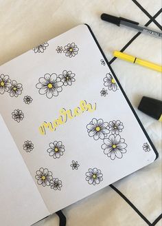 an open notebook with flowers and the word march written in yellow on it next to markers