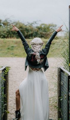 a woman in a white dress is standing on a bridge with her arms spread out