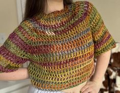 a woman wearing a multicolored crochet top with her hands on her hips