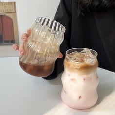 a woman is holding two iced drinks in front of her