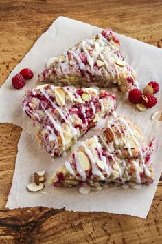 three pieces of cake sitting on top of a piece of paper with nuts and raspberries