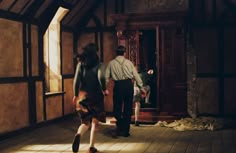 a man and woman walking down a hallway in an old fashioned building with wood floors