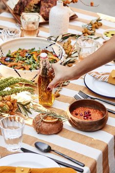 a person pouring olive oil on top of a table covered in plates and bowls filled with food