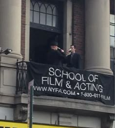 two men standing on the balcony of a building with a sign that says school of film and acting