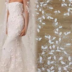 a woman in a wedding dress and veil standing next to a wall with flowers on it