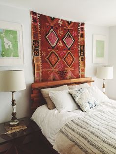 a bed with white sheets and pillows in front of a colorful tapestry on the wall