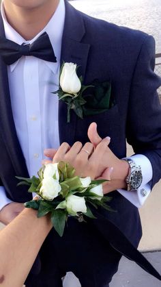 two people in tuxedos are holding hands with white roses on their lapels