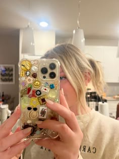 a woman taking a selfie with her cell phone case covered in buttons and charms