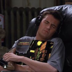 a man laying in a chair with headphones on reading a book and listening to music