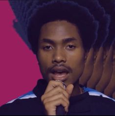 a man with dreadlocks standing in front of a pink background