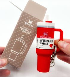 a person holding a red coffee mug shaped like a travel mug with a keychain attached to it