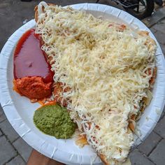 a person holding a paper plate with some type of pizza and sauces on it