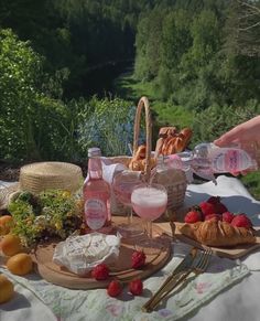 a picnic table with food and drinks on it, including breads, fruit, wine glasses and strawberries