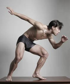 a man with no shirt is standing on top of a wooden table and stretching his arms