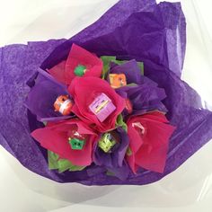 a bouquet of flowers wrapped in purple tissue paper with candy cubes and candies