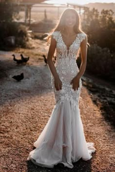 a woman in a white wedding dress standing on a dirt road with ducks behind her