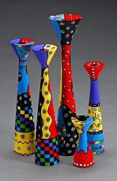 four colorful vases are arranged in a row on a gray surface, one is brightly colored and the other is decorated with polka dots