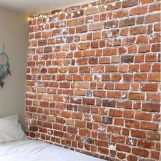 a brick wall in the corner of a room with white sheets and pillows on it