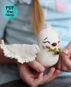 a person holding a white crocheted bird with wings and a flower in it's mouth