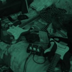 a guitar and other musical equipment on a bed in a room with green light from the window