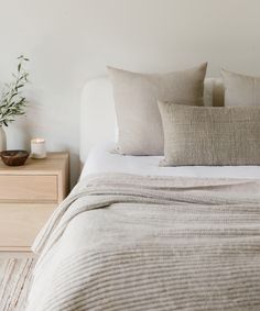 a bed with two pillows on top of it next to a night stand and vase