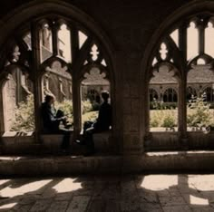 two people sitting on a bench in the middle of an old building with arched windows