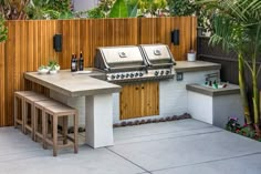 an outdoor kitchen with two grills and three stools next to the counter top