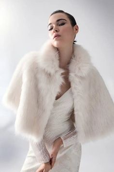 Dress the party: receive 20% off when purchasing four or more bridal styles. Use code BRIDAL20 at checkout. Luxurious and chic, this gorgeous cape is made from the most premium faux fur and features a wide collar with a concealed hook & eye closure in the front. Perfect for a black-tie event or regular wear, this cozy cape is the perfect layering piece for a girl with ethical fashion in mind. This garment is a one-size-fits-all. Elegant White Capelet With Cape Sleeves, Fitted Cape-style Party Outerwear, Fitted Party Cape Outerwear, Fitted Cape Outerwear For Party, Chic White Cape Outerwear, Luxury Cream Outerwear For Evening, Elegant Winter Capelet With Cape Sleeves, Winter Ceremony Long Sleeve Outerwear, Cream Winter Wedding Outerwear