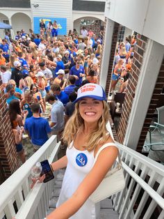 a woman in a white shirt and blue hat standing on a porch next to a crowd of people