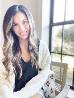 a woman sitting on a bench in front of a window with her arms crossed and smiling at the camera