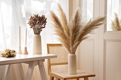 two vases with dried plants in them sitting on a table next to a chair