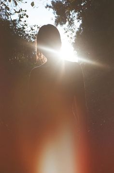 a person standing in front of trees with the sun shining through their back and behind them