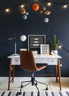 a desk with a chair and a computer on it in front of a space themed wall