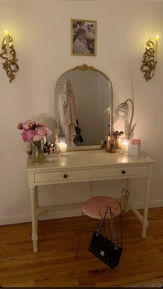 a dressing table with a mirror, stool and flowers on it in front of a white wall