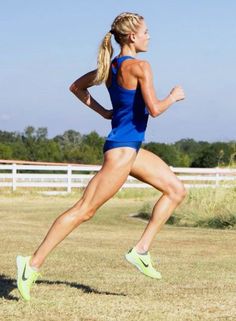 a woman running in the grass with her back turned to the camera and she is wearing a blue tank top