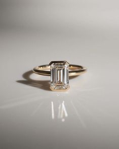 an emerald - cut diamond ring sits on a white surface in front of the camera