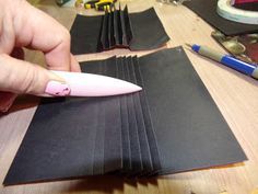 a person is cutting out black paper with a pink object in the foreground and other craft supplies behind them