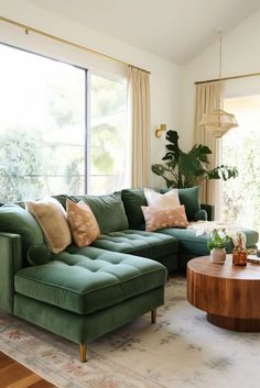 a living room filled with green couches next to a wooden table and large windows