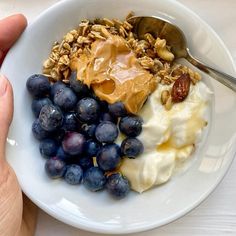 a white bowl filled with yogurt, granola and blueberries