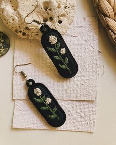 two black earrings with white flowers on them sitting next to a rock and sea shell