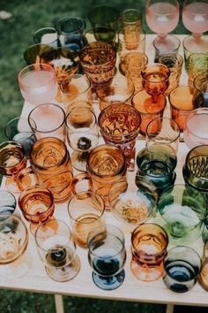 many different colored glasses sitting on top of a wooden table in front of some grass