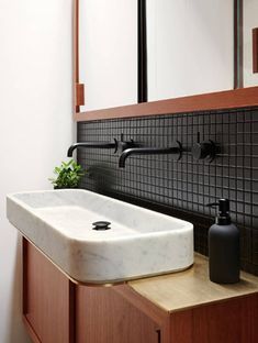 a bathroom sink sitting under a mirror next to a wooden cabinet and black tile on the wall