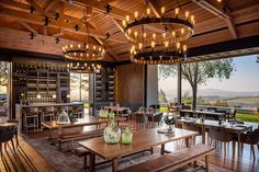 an empty restaurant with wooden tables and wine bottles hanging from the ceiling, along with lots of windows