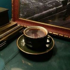 a cup of coffee sitting on top of a saucer next to a painting and a piano