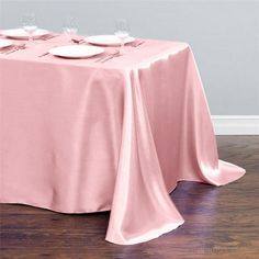 a pink table cloth with white plates on it and two empty wine glasses sitting at the end