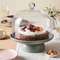 a cake under a glass dome on top of a table with plates and glasses next to it